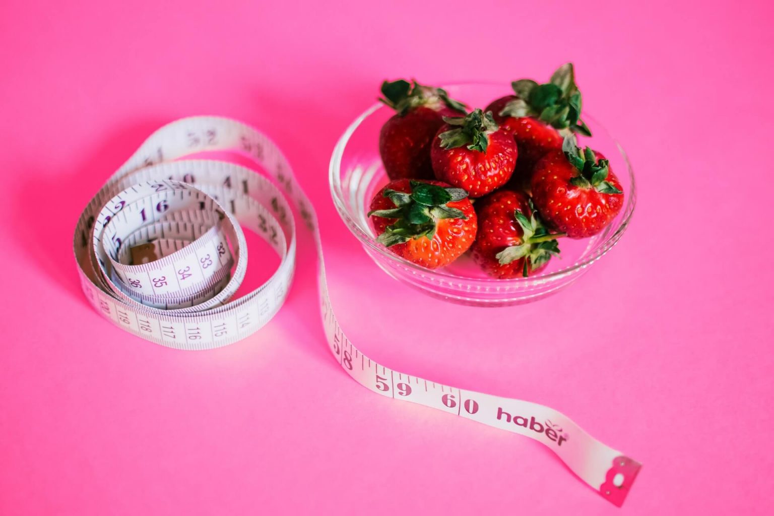 A cup of strawberries next to a tape measure